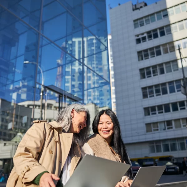 cheerful-women-with-laptops-sitting-on-street-step-2025-03-08-14-14-19-utc